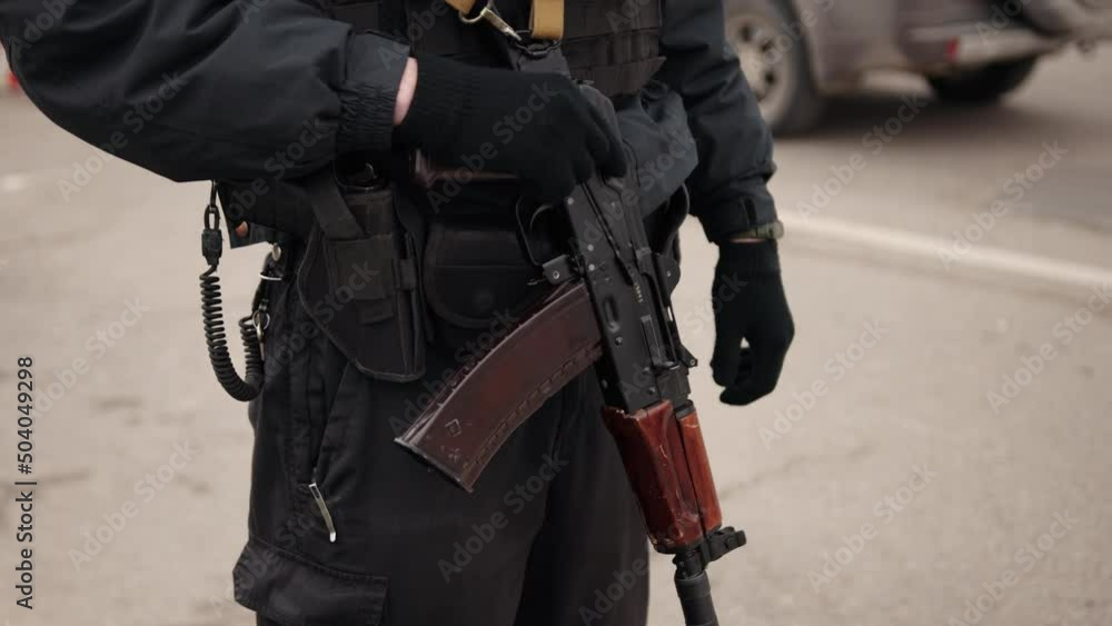 Members of police strategic response group stand guard. Man in black military uniform holds machine gun, standing outsdoor. Control point. Policeman stands with machine gun controlling car traffic Members of police strategic response group stand guard. Man in black military uniform holds machine gun, standing outsdoor. Control point. Policeman stands with machine gun controlling car traffic