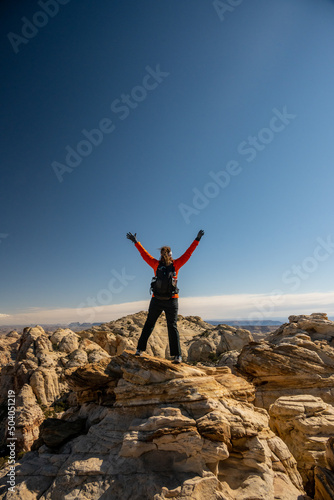 Woman In Orange Jacket Power Poses In Desert Rocks