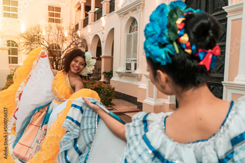 Two young Latina women, one mestizo and one Hispanic, dancing in traditional Nicaraguan costumes outside a colonial house