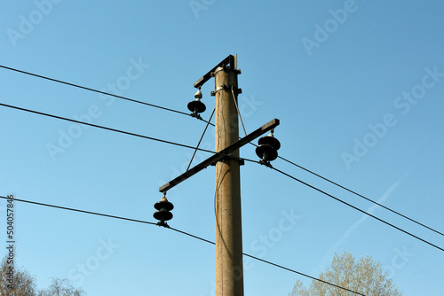 The top of a reinforced concrete pole with a passing power line against a blue clear sky.