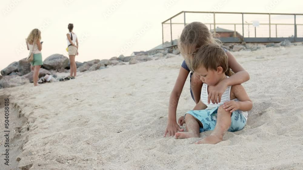 Girl helping her little brother to look for seashells in the sand on the coast Girl helping her little brother to look for seashells in the sand on the coast