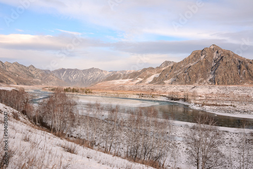 The not completely frozen bed of a beautiful winding river flowing through a snow-covered valley surrounded by mountains.