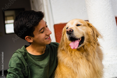 latino teenager laughing with his golden retriever dog sitting in the driveway