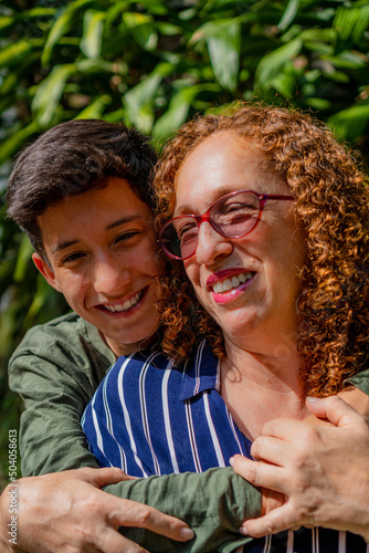 middle-aged latina mother with her teenage son hugging. laughing in the nature on a sunny day. vertical photo