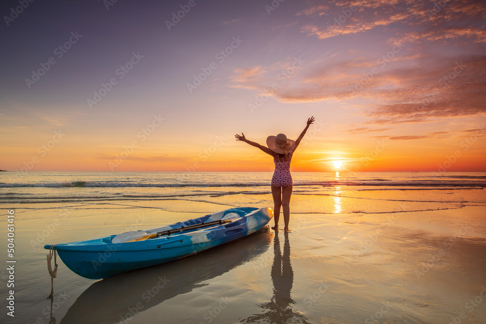 Fototapeta premium Young lady tourist and canoe on the beach with sunset on the sea at Phuket province, Thailand.