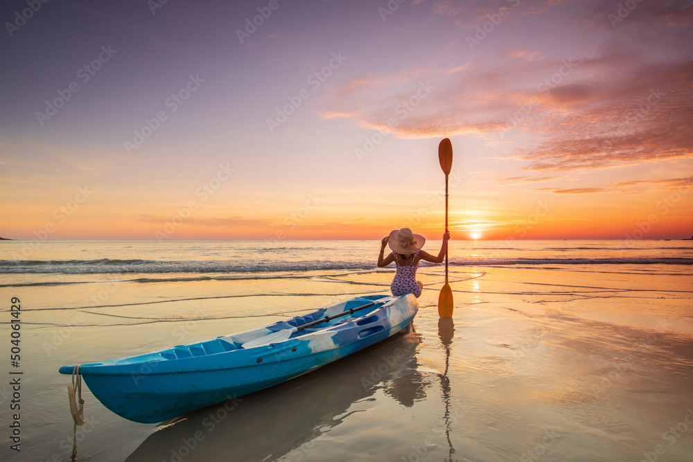 Young lady tourist and canoe on the beach with sunset on the sea at Phuket province, Thailand.