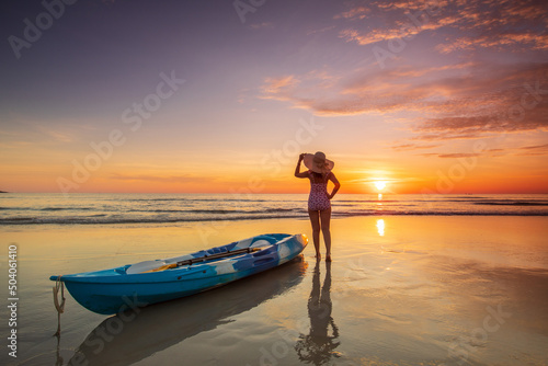Young lady tourist and canoe on the beach with sunset on the sea at Phuket province, Thailand. © Nakornthai