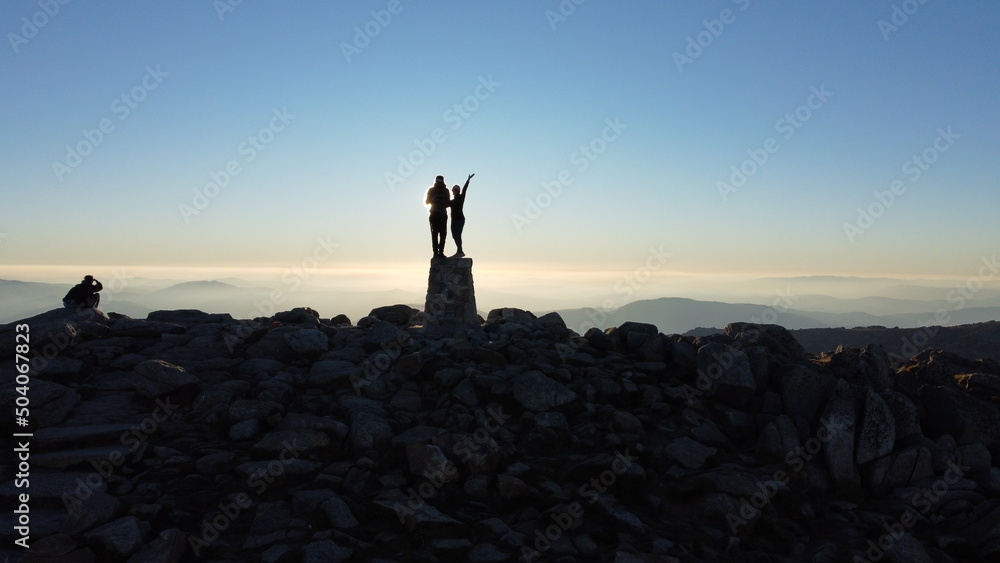 silhouette of a couple standing on a rock, on top of mountains, at sunset or sunrise, high energy and motivation, on top of rocks, on peak of mountain & blue orange sky