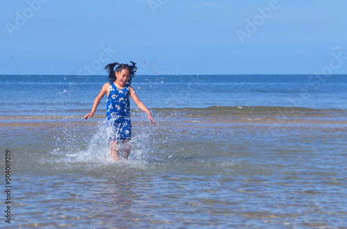 Happy Asian child girl is jumping in sea water
