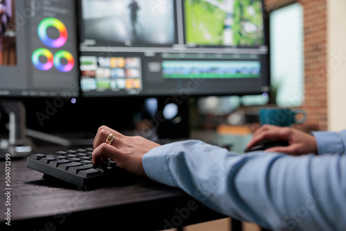 Close up shot of digital video editor sitting at multi monitor workstation desk while working on movie footage. Creative post production house videographer improving film frames visual quality. photo