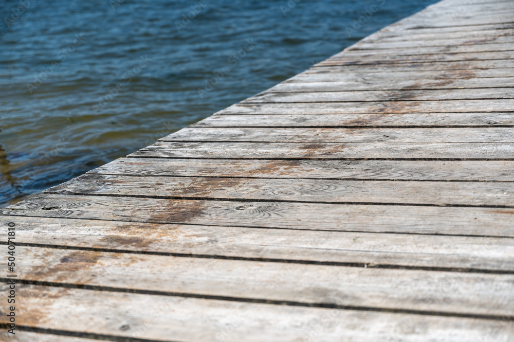Fototapeta premium The weathered planks of the pier against the water. The old planks of the small pier on the shore. Close-up. Selective focus.