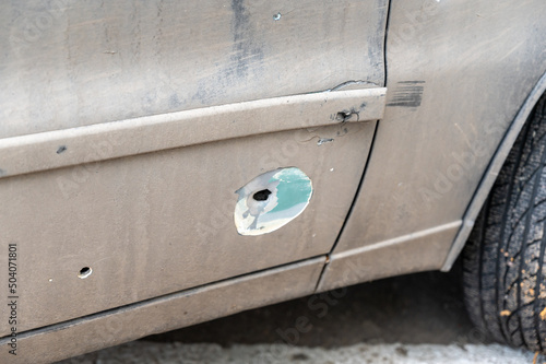 A car shelled during the war. Through holes from shrapnel and bullets on the car door. Russian attack on Ukraine in 2022. Shelling of civilians. War crimes concept