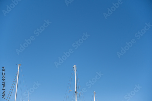 Upper section of sea yachts against the blue sky. White masts of sea yachts, standing at the pier in the seaport.