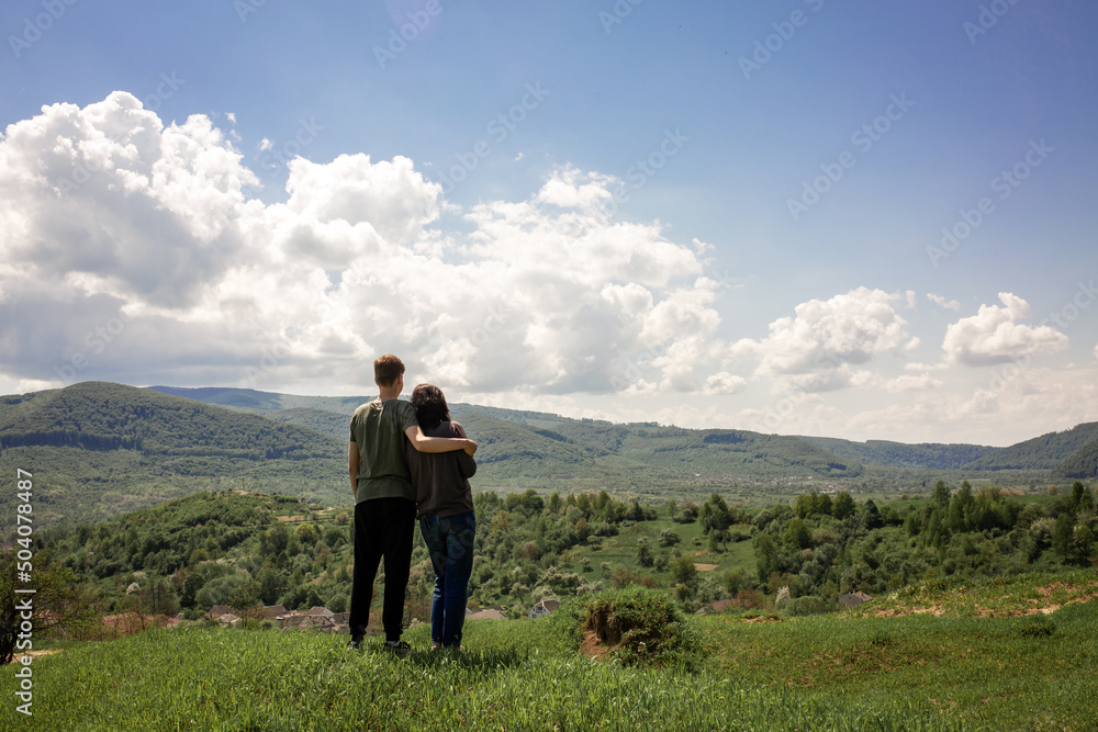 The guy hugs the girl. The guy and the girl look at the mountain landscape.