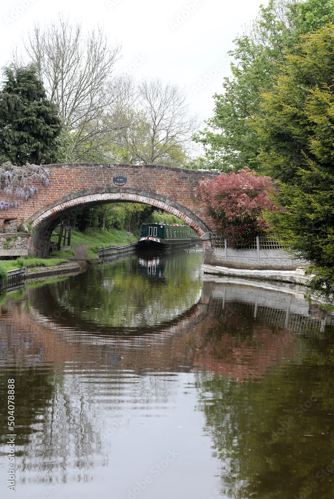 Tranquil setting showing canal with boats, bridge, plants and ducks.