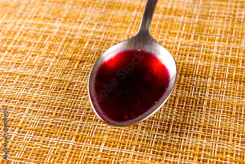 table spoon with red liquid on a light brown clipped background, kitchen concept photo