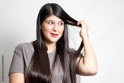 Overweight Latin young adult woman shows how silky and shiny her black hair is, very long, straight, which she takes in her hands, very happy and proud of the beautiful hair with a beautiful haircut 