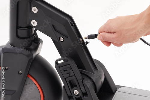 Battery charging process of black electric motorized scooter on a white background. Hand connects the cable to e-scooter. Close up.