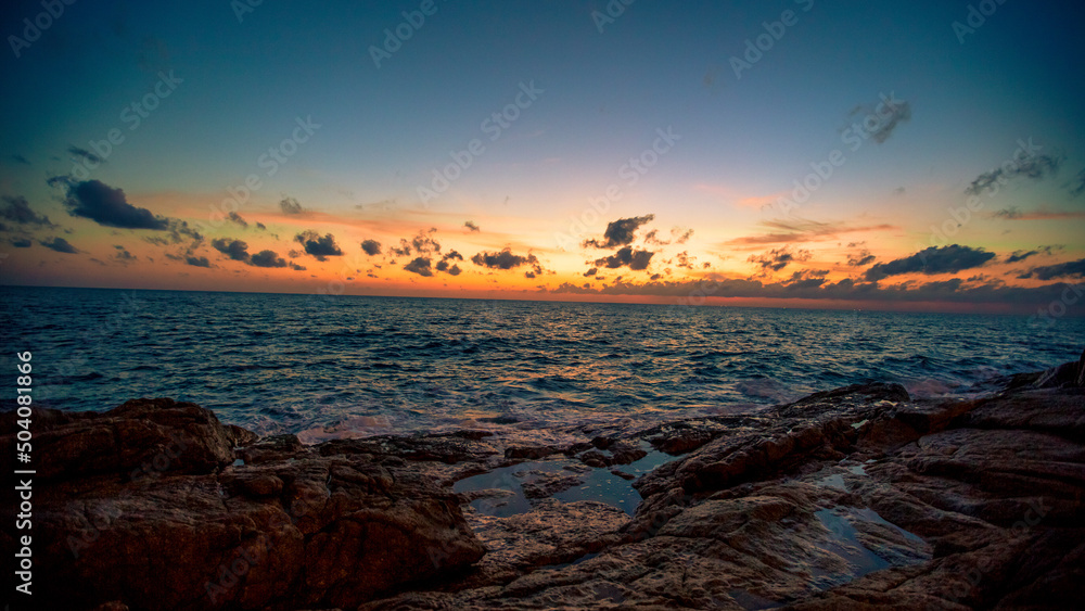 Obraz premium Blurred nature background of the morning sun by the sea, a beautiful golden light, among the trees, rocks and local fishing boats, the beauty of nature during the day.