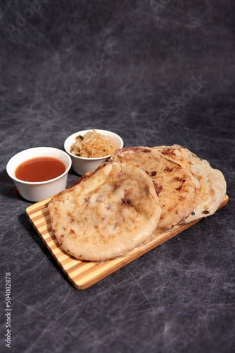 Pupusas on a wooden board with curtido and sauce over a black marble background
