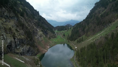 Reflective panoramic alpine lake in a Swiss mountain valley, aerial backwards