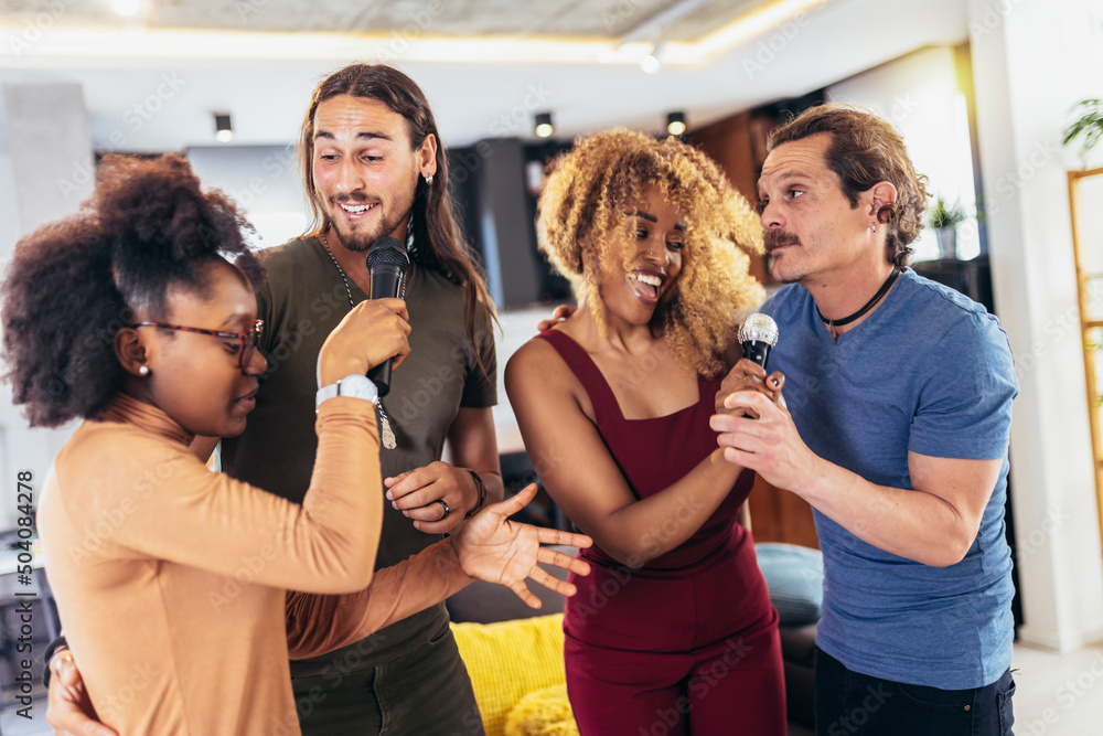 Obraz premium Group of young multicultural friends having party singing song using microphone at home.