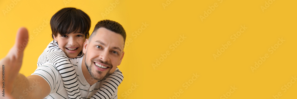 Father and his little son taking selfie on yellow background with space for text Father and his little son taking selfie on yellow background with space for text