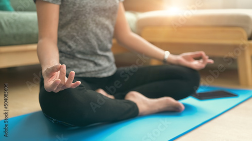Peaceful young woman in sports clothes practicing yoga, sitting on fitness mat in lotus position. Yoga concept.