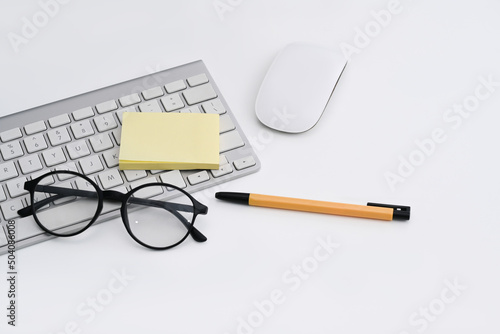 Eyeglasses  sticky note  wireless keyboard ad mouse on white office desk.