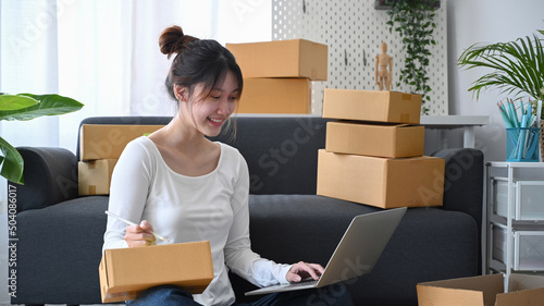 Happy start up small business owner sitting on floor and checking online order on laptop. © Prathankarnpap