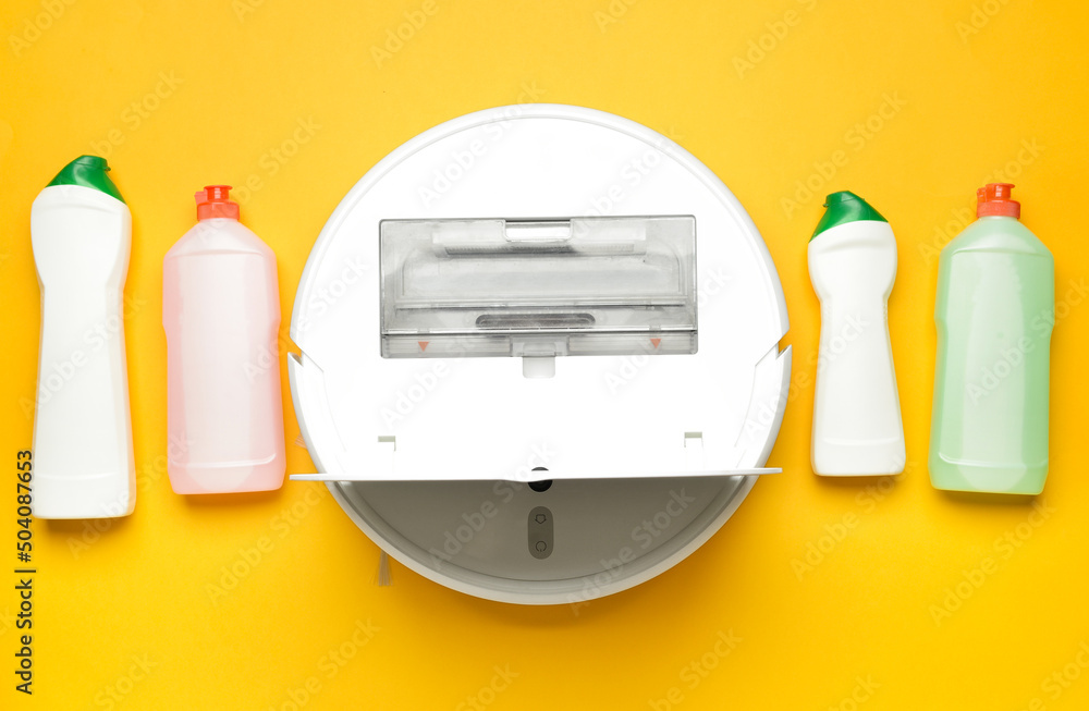 Bottles of different detergents and open robot vacuum cleaner on color