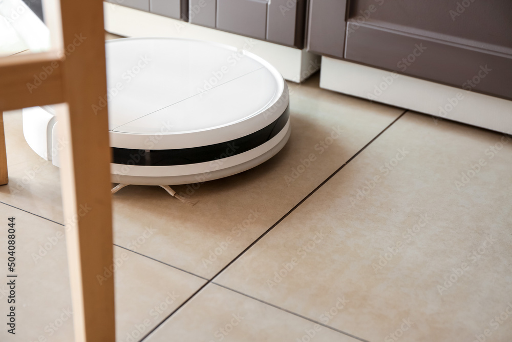 Modern robot vacuum cleaner on floor in kitchen Modern robot vacuum cleaner on floor in kitchen