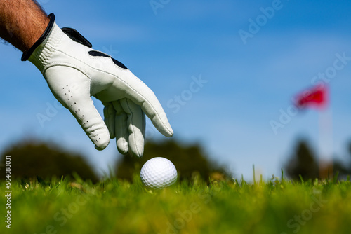 Golfer man with golf glove. Hand putting golf ball on tee in golf course.