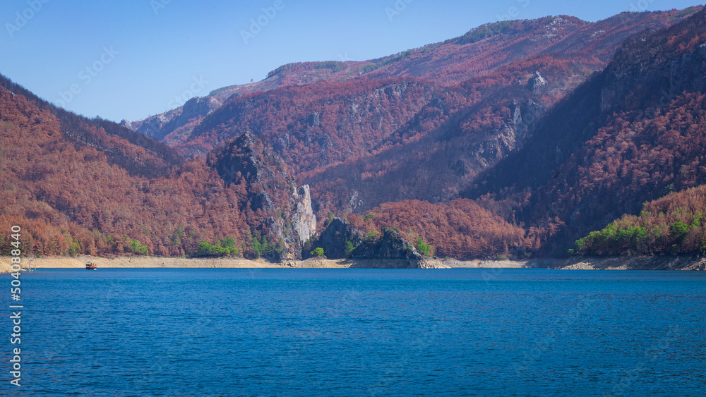 View of the green water of Oymapinar Dam with red trees on the shore