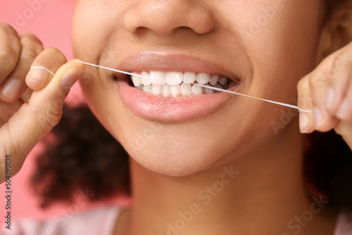 African-American teenage girl flossing teeth on pink background  closeup