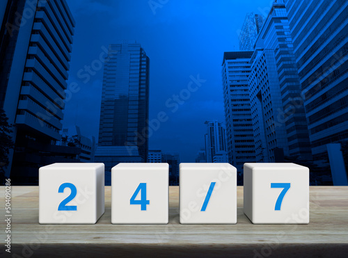 24/7 letter on white block cubes on wooden table over modern office city tower and skyscraper, Business full time service concept