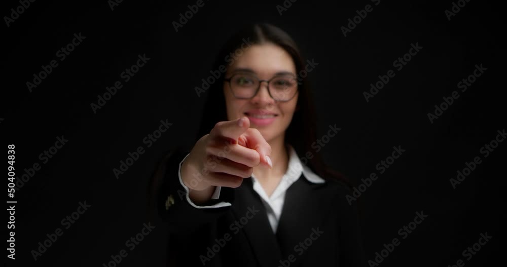 Businesswoman with long hair points directly at the camera chooses you, smiles broadly, wears glasses and a white shirt and jacket highlighted on a black background.Selects a candidate, invites people Businesswoman with long hair points directly at the camera chooses you, smiles broadly, wears glasses and a white shirt and jacket highlighted on a black background.Selects a candidate, invites people
