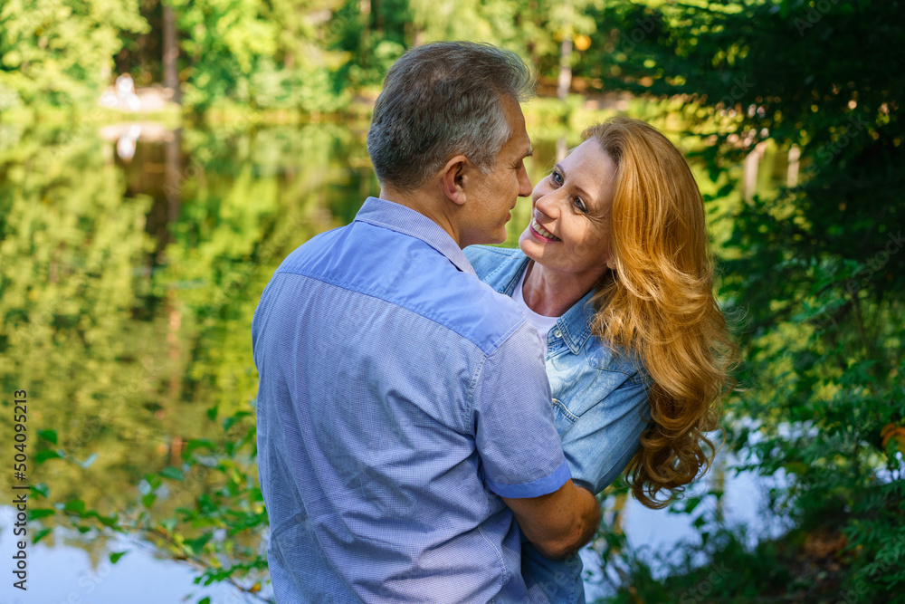 Happy mature couple embracing and embracing in thickets headland near lake are smiling with happiness on a sunny summer day. Caucasian man and woman spend free time together