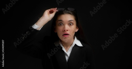 Shocked businesswoman raises her glasses in surprise against an isolated black background. He opens his mouth, can't believe his eyes. Unexpected news