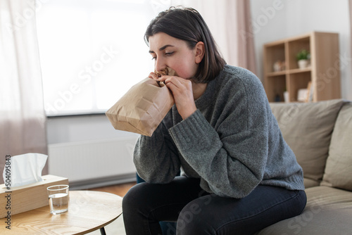 mental health and psychological problem concept - woman having panic attack breathing to bag at home photo