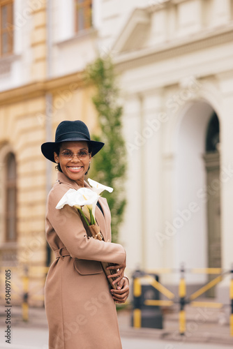Portrait of an African woman, enjoying outside, wearing a hat and holding flowers.