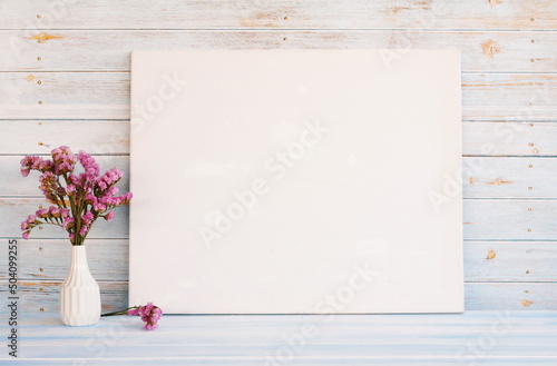 White canvas hanging on light blue wooden wall. Mockup, wall decor, blank canvas stretched on stretcher bar