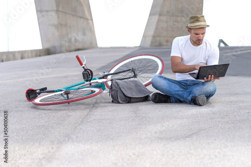 young man, sitting on ground with legs crossed and working on laptop while resting photo