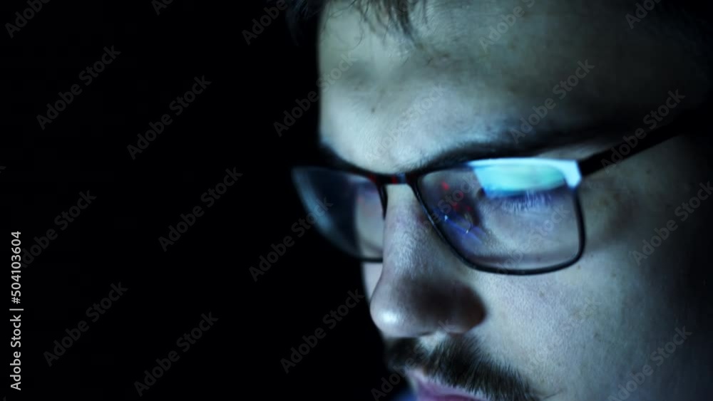 Very tired nerdy student with glasses is sitting at darkness browsing internet, closeup face. Closeup reflection in glasses of man browsing website on computer in dark Very tired nerdy student with glasses is sitting at darkness browsing internet, closeup face. Closeup reflection in glasses of man browsing website on computer in dark