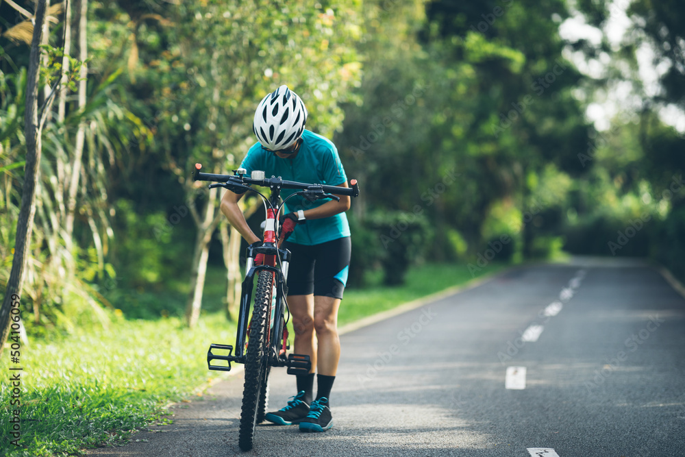 Woman cyclist adjust the seat height cycling on summer park trail Woman cyclist adjust the seat height cycling on summer park trail