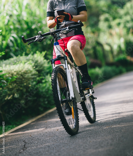 Woman using smart phone cycling on tropical park trail in summer