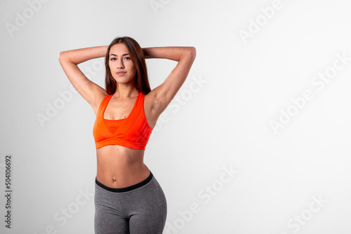a girl in a bright sports top, hands behind her head on a white background. © maxfotoadobe