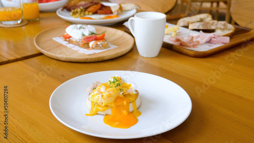 Cut egg benedict with liquid yolk on english muffin in restaurant. Classic poached egg with hollandaise sauce sandwich on white plate on table in cafe. Breakfast, lunch or brunch set food concept.