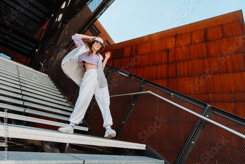 Bild auf Leinwand Fashion cutte woman with sunglasses and hat dancing outside looking at camera