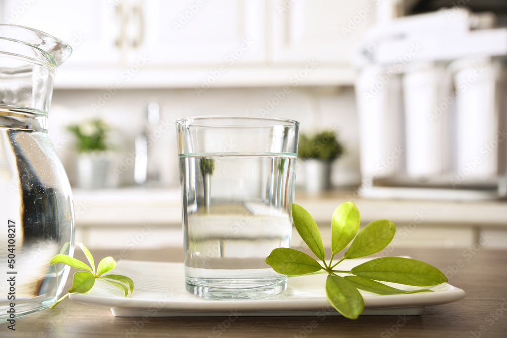 Glass of purified water and jug on kitchen bench closeup - obrazy, fototapety, plakaty 